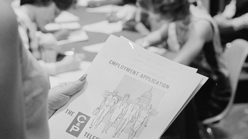 Close-up image of a woman's hands holding a job application package for a telephone company.