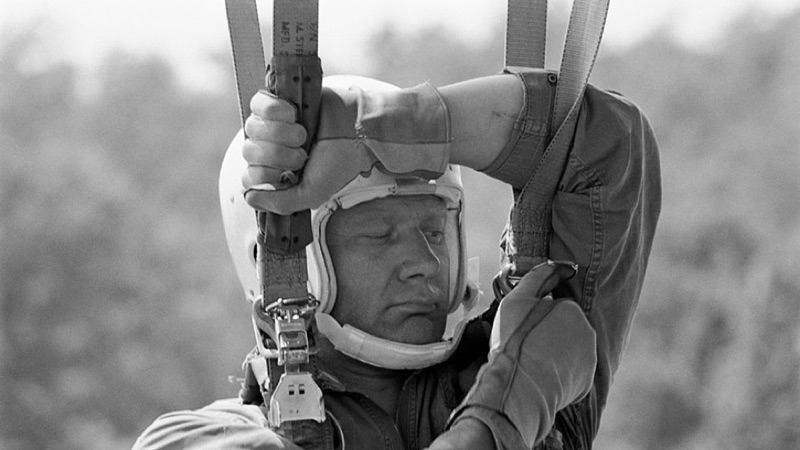 Buzz Aldrin about to unhook himself from parachute webbing that's supporting him in mid-air.